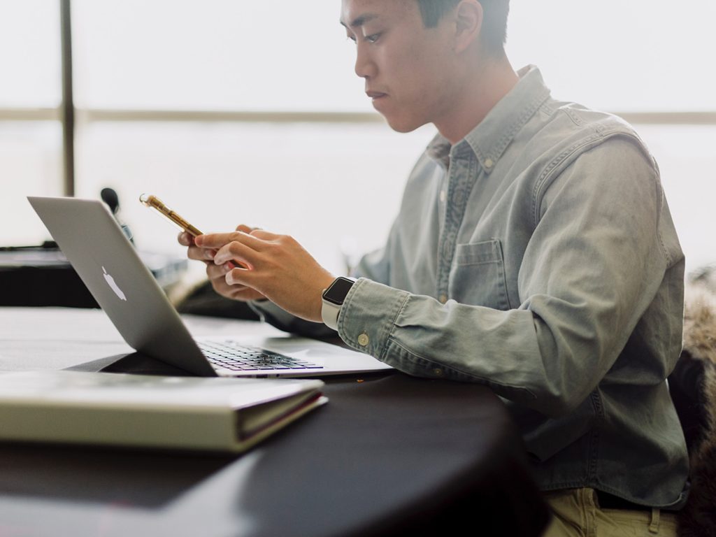 University Student On iPhone In Front Of MacBook Air